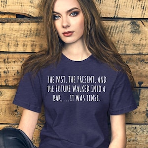 May include: A navy blue t-shirt with white text that reads "THE PAST, THE PRESENT, AND THE FUTURE WALKED INTO A BAR....IT WAS TENSE."