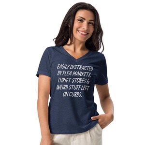 May include: Navy blue V-neck t-shirt with white text: "EASILY DISTRACTED BY FLEA MARKETS, THRIFT STORES & WEIRD STUFF LEFT ON CURBS." The shirt is made of a soft material.