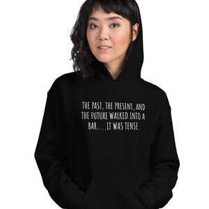 May include: Black hooded sweatshirt with white text that reads "THE PAST, THE PRESENT, AND THE FUTURE WALKED INTO A BAR....IT WAS TENSE."