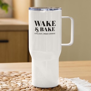 Puede incluir: Un termo blanco con asa y tapa transparente. El termo presenta el texto "WAKE & BAKE" en negro, con la frase "(CHILL OUT, I MAKE COOKIES)" debajo. El termo está sobre una esterilla tejida.