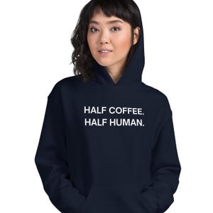 May include: A navy blue hoodie with the text "HALF COFFEE. HALF HUMAN." printed in white on the front.