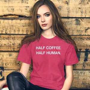 May include: A woman wearing a red heather t-shirt with the text "HALF COFFEE. HALF HUMAN." printed in white.