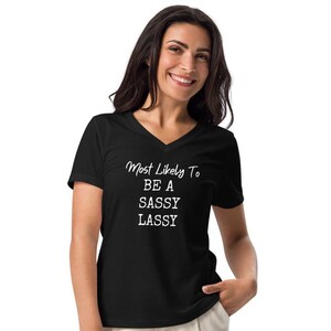 May include: Black v-neck t-shirt with white text that reads "Most Likely To Be A Sassy Lass"