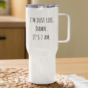 Könnte beinhalten: Weißer Reisebecher mit Griff und transparentem Deckel. Auf dem Becher steht in schwarzer Schrift: "I'M JUST LIKE, DAMN. IT'S 7 AM." Der Becher steht auf einer gewebten Matte.