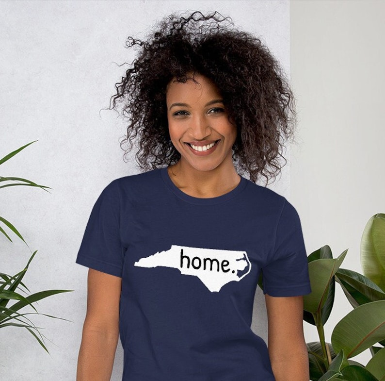 May include: A navy blue t-shirt with a white outline of the state of North Carolina and the word "home." printed inside the outline.