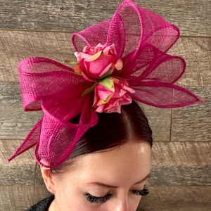 May include: A pink and green floral hair accessory with a large bow made of pink mesh fabric.