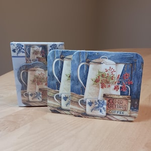 May include: Set of four blue and white ceramic coasters featuring a vintage coffee pot and cups with a red berry design. The coasters have a wooden background and a tin can with the text "Good Morning Coffee".