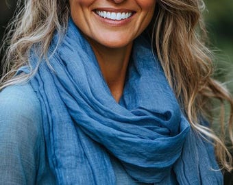 May include: A lightweight blue scarf with a soft, crinkled texture draped around the neck. The fabric has a semi-sheer appearance and a consistent medium blue color throughout, featuring loose folds and a natural, relaxed drape across the chest.