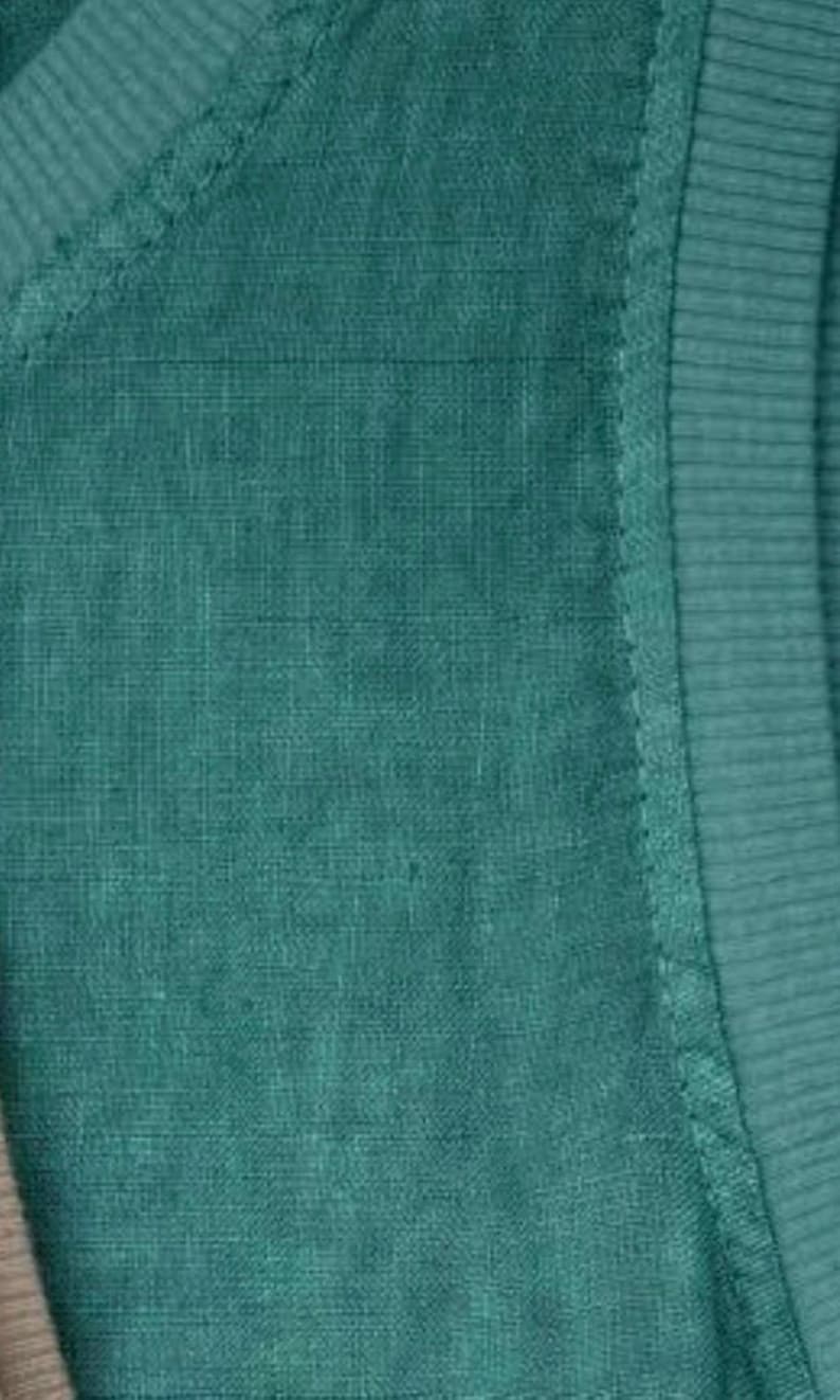 Pu&ograve; includere: Un capo di abbigliamento verde ottanio caratterizzato da una superficie in tessuto intrecciato e testurizzato. Il pezzo presenta un dettaglio a coste sul colletto o sul bordo, con cuciture visibili che collegano la sezione a coste al corpo principale.