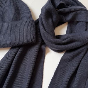 May include: A dark navy blue knitted beanie hat and scarf set. The beanie has a folded brim and the scarf is long and rectangular. Both items have a ribbed texture and are made of a soft material.