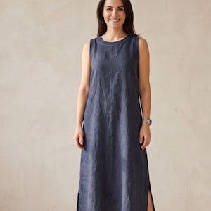 Pu&ograve; includere: Un abito midi senza maniche in un colore blu scuro a tinta unita. Il capo presenta uno scollo rotondo con un bordo a coste spesso e spacchi laterali dritti sull'orlo. Il tessuto ha una trama visibile, che offre una silhouette rilassata.