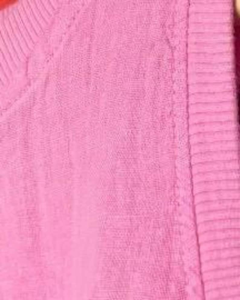 Pu&ograve; includere: Un capo senza maniche di colore rosa acceso caratterizzato da una texture in tessuto intrecciato. L'articolo presenta un colletto in maglia a coste e un bordo in maglia a coste abbinato lungo lo scalfo, con cuciture uniformi e tinta unita.