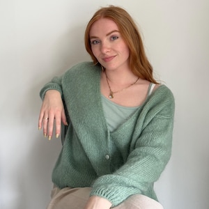May include: A light green, button-down cardigan with a soft, textured appearance. The cardigan is paired with a light green tank top and a gold necklace. The overall aesthetic is casual and comfortable.