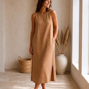 Pu&ograve; includere: Un abito midi senza maniche di colore marrone chiaro uniforme. Il capo presenta uno scollo rotondo, una silhouette dritta e rilassata e uno spacco laterale verticale lungo l'orlo inferiore. Il tessuto ha una trama visibilmente testurizzata.