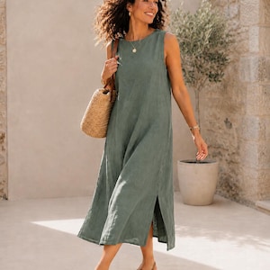 Pu&ograve; includere: Un abito midi senza maniche color verde salvia con scollo rotondo e spacchi laterali sull'orlo. L'abito &egrave; abbinato a una borsa in paglia intrecciata e sandali in pelle marrone. Il capo presenta una silhouette dritta e rilassata.