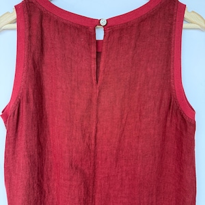 Pu&ograve; includere: Un top senza maniche di colore rosso intenso con tessuto testurizzato, scollo rotondo a coste e ampi giromanica a coste. Il retro presenta una cucitura verticale e una piccola apertura a goccia chiusa da un bottone di colore chiaro.