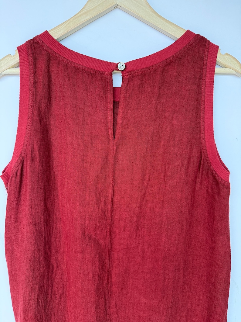 Pu&ograve; includere: Un top senza maniche di colore rosso intenso con tessuto testurizzato, scollo rotondo a coste e ampi giromanica a coste. Il retro presenta una cucitura verticale e una piccola apertura a goccia chiusa da un bottone di colore chiaro.