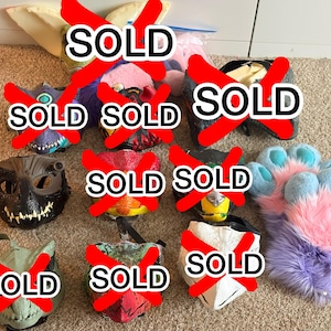 May include: A collection of animal-themed masks and a pair of plush paw gloves. The masks feature various textures and colors, including black, green, and red. One pair of fuzzy gloves has light blue paw pads and a purple and pink fur exterior.