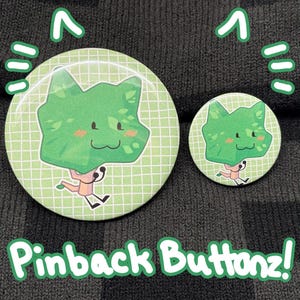 Pode incluir: Dois botões redondos verdes com um personagem de desenho animado. O personagem tem uma cabeça verde e frondosa com pernas correndo. O texto "Pinback Buttonz!" é verde.