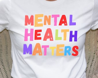 May include: White t-shirt with the text "MENTAL HEALTH MATTERS" in rainbow colors.