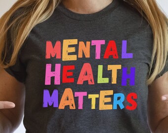 May include: A dark gray t-shirt with the text "MENTAL HEALTH MATTERS" printed in rainbow colors. The text is in a bold, blocky font.