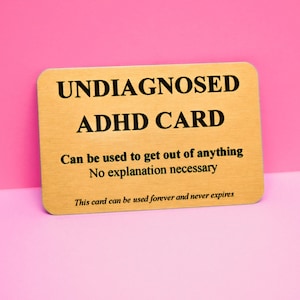 May include: A rectangular gold-coloured card with black text that reads: UNDIAGNOSED ADHD CARD, Can be used to get out of anything, No explanation necessary, This card can be used forever and never expires. The card has a brushed metallic finish.