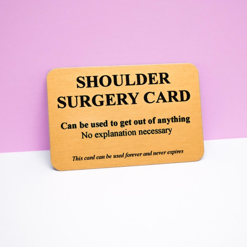 Op de afbeelding: Een rechthoekige goudkleurige metalen kaart met afgeronde hoeken en zwarte tekst die luidt: SHOULDER SURGERY CARD, Can be used to get out of anything, No explanation necessary, en This card can be used forever and never expires.