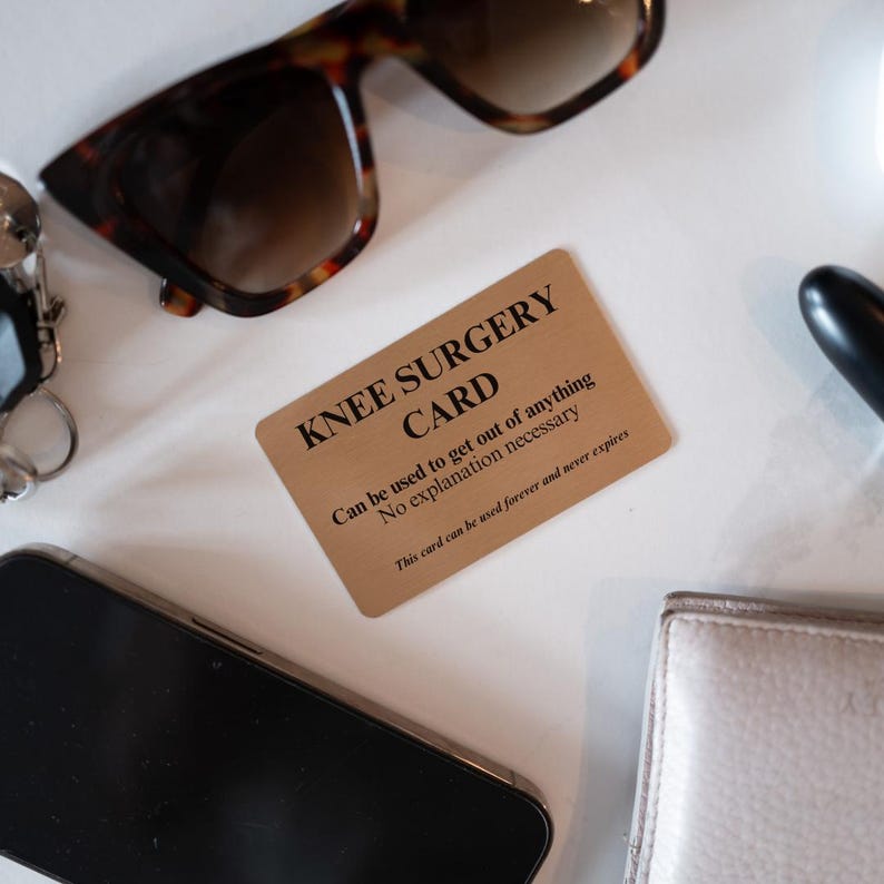 Op de afbeelding: Een rechthoekige goudkleurige metalen kaart met zwarte tekst die luidt KNEE SURGERY CARD, Can be used to get out of anything, No explanation necessary, en This card can be used forever and never expires, omringd door een zonnebril.