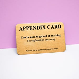 Puede incluir: Una tarjeta rectangular de metal dorado con esquinas redondeadas que presenta texto negro que dice: APPENDIX CARD, Can be used to get out of anything, No explanation necessary, y This card can be used forever and never expires.