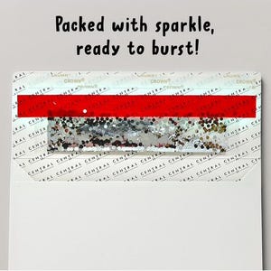 Op de afbeelding: Een witte envelop met een rechthoekige kaart met de tekst Packed with sparkle, ready to burst! De kaart heeft een horizontale rode streep boven een sectie gevuld met zilveren en gouden glitters, tegen een achtergrond van het herhalende Central Crown logo.