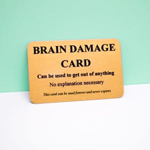 Puede incluir: Una tarjeta rectangular de color dorado con esquinas redondeadas que presenta texto negro que dice: BRAIN DAMAGE CARD, Can be used to get out of anything, No explanation necessary, This card can be used forever and never expires.