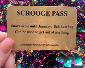 Puede incluir: Una tarjeta "Scrooge Pass" dorada con texto negro, sobre un fondo de oropel colorido. La tarjeta dice "No disponible hasta enero. Bah humbug. Se puede usar para salir de cualquier cosa. Se renueva automáticamente cada 1 de diciembre."