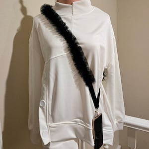May include: White sweatshirt with a black lace trim and a black phone strap with a gold phone case attached.