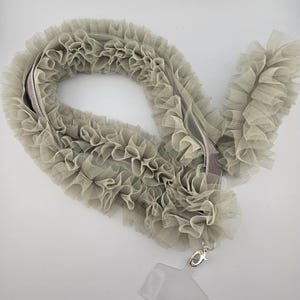 May include: A light gray ruffled fabric lanyard with a silver clasp and a clear plastic badge holder.