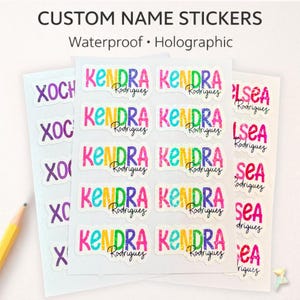 May include: A sheet of custom name stickers featuring the name Kendra Rodriguez in a colorful, holographic, multi-colored font. The text CUSTOM NAME STICKERS Waterproof Holographic is printed at the top. A yellow pencil is visible on the left.