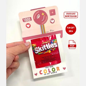 May include: Printable card with a pink and white camera design. The card says "You add color to my world" and has a small pouch for a bag of Skittles candy. The text "1000" is visible on the camera.
