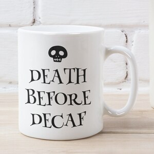 May include: White ceramic coffee mug with a black skull and the text "DEATH BEFORE DECAF".