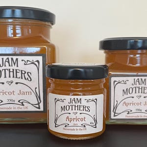 May include: Three glass jars of apricot jam, labelled "JAM MOTHERS" with different sizes. The largest jar is 330g, the middle jar is 85g, and the smallest jar is 150g. All jars have a black lid and are filled with a bright orange jam.