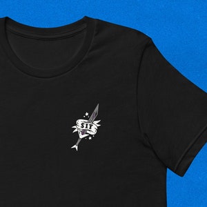 May include: Black t-shirt with a small graphic of a sword piercing a heart with the word "SIT" on a banner.