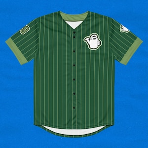 Pode incluir: Camisola de beisebol verde com riscas brancas e um gráfico de regador branco na frente. A camisola tem um fecho de botões na frente e mangas curtas.