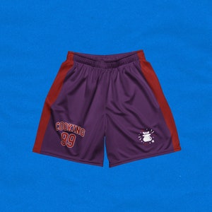 May include: Purple athletic shorts with red side panels. The shorts have "COOKING 99" printed on the left leg and a white graphic of a pot with a spoon on the right leg.