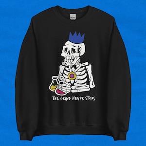 May include: Black sweatshirt with a graphic of a skeleton wearing a blue crown and holding beakers. The text "THE GRIND NEVER STOPS" is printed below the skeleton.