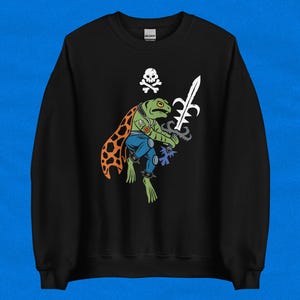 May include: Black sweatshirt with a green frog wearing a blue and orange costume holding a sword. The frog has a skull and crossbones on its chest.