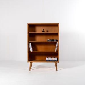 Puede incluir: Una estanter&iacute;a de madera de estilo moderno de mediados de siglo con cuatro estantes. La estanter&iacute;a es de color marr&oacute;n claro y tiene un dise&ntilde;o minimalista. Contiene libros y objetos decorativos. La estanter&iacute;a mide 122 cm de alto.