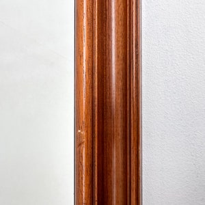 May include: Close-up of a wooden frame with a dark brown finish. The frame has a raised, decorative edge.