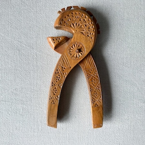May include: A wooden nutcracker carved with intricate geometric patterns. The nutcracker is shaped like a bird's head with a beak that opens and closes to crack nuts.