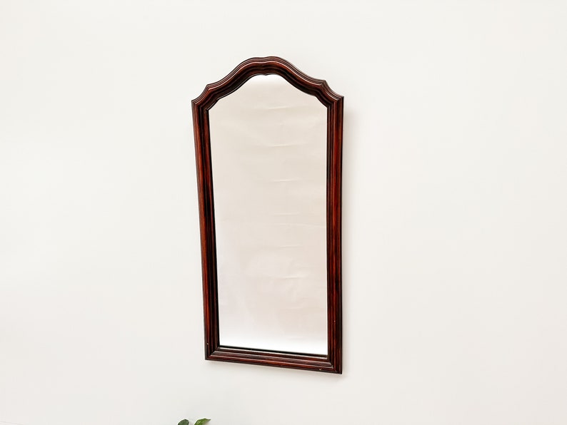 May include: A dark wood framed mirror with a beveled edge and an arched top.