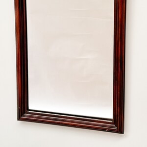 May include: A rectangular mirror with a dark wood frame. The frame has a simple, traditional design with a smooth finish.