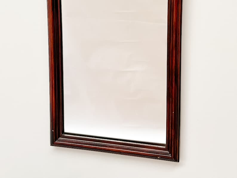 May include: A rectangular mirror with a dark wood frame. The frame has a simple, traditional design with a smooth finish.