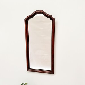 May include: A mahogany wood framed mirror with a beveled edge and an arched top.